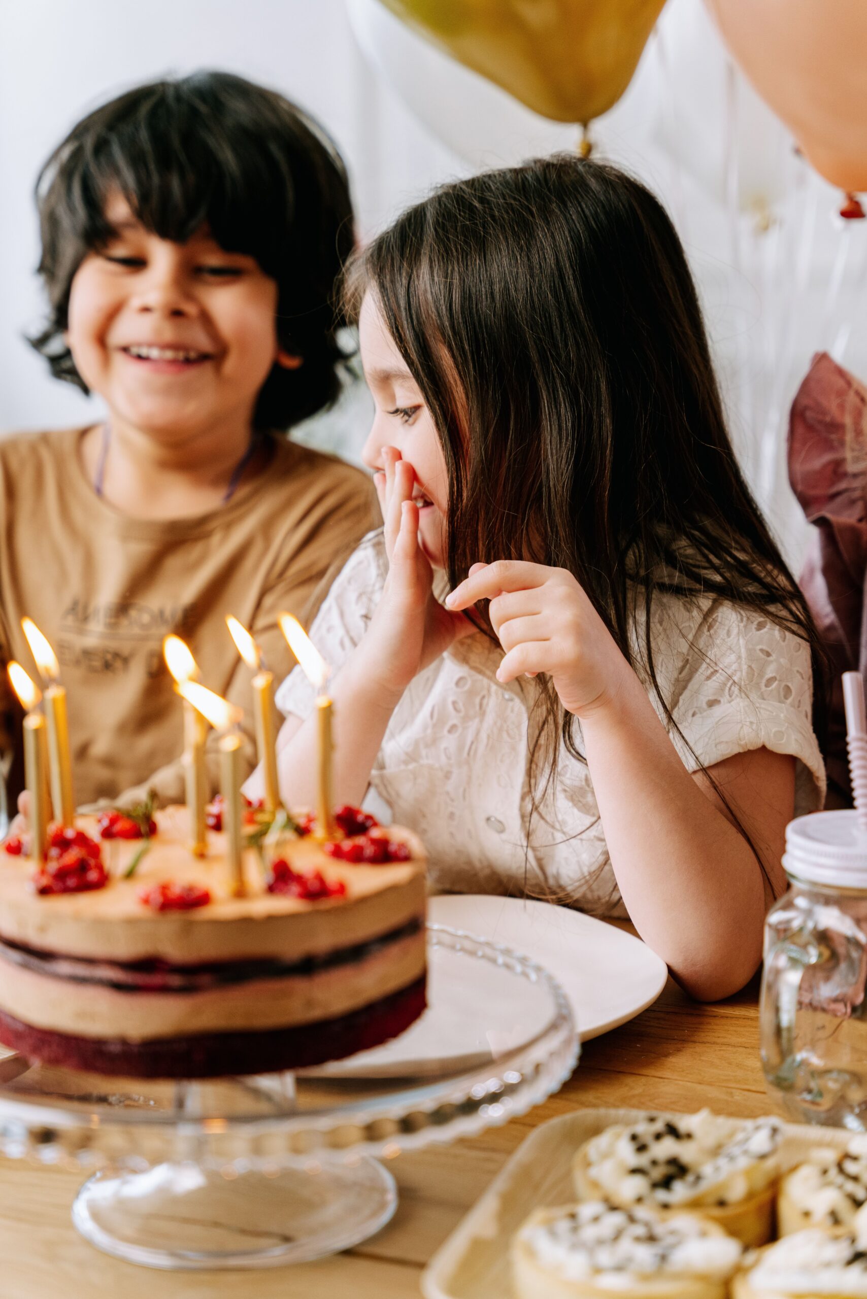 Children joyfully celebrate a birthday with a cake adorned with lit candles, ready for a wish.